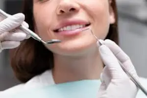 Close-up of a smiling patient during a dental appointment, showcasing dental tools used for oral examination and treatment.