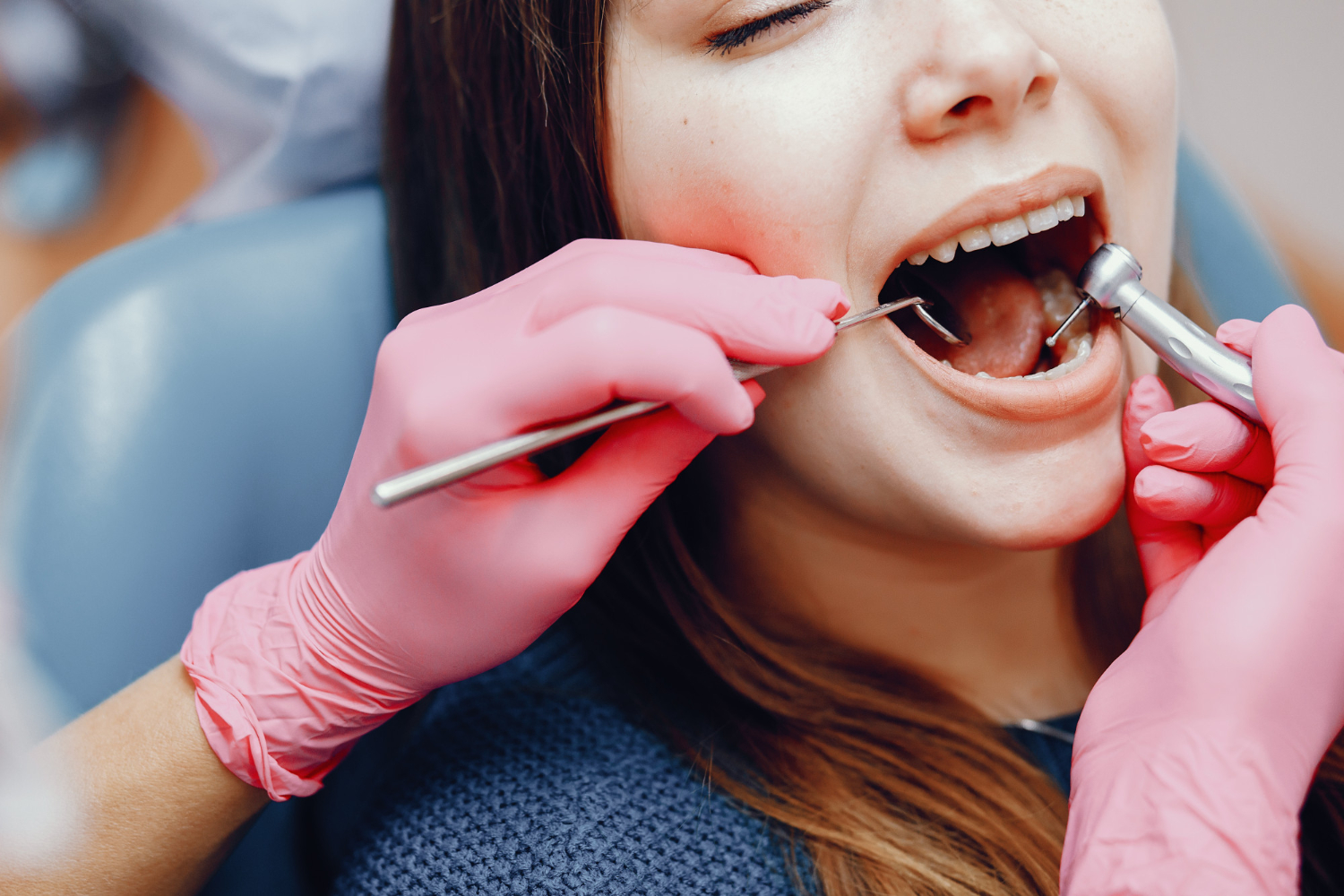 Dentist examining a patientโs teeth using a dental mirror and handheld instrument during an oral examination.
