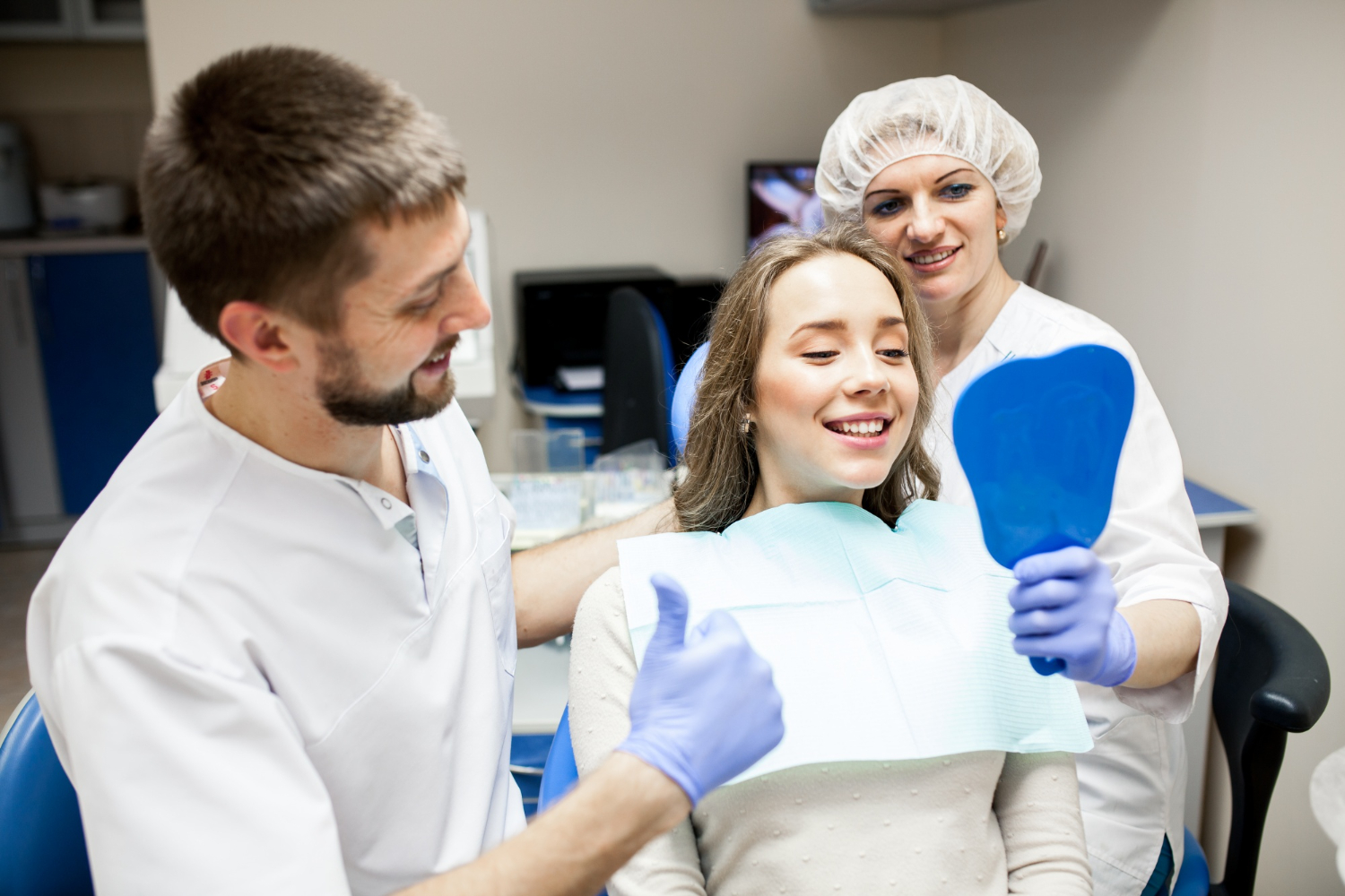 Dentist and dental assistant assisting a smiling patient during a dental examination in a dental office.