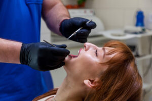 Dentist performing an oral examination to assess mouth tissue during an oral biopsy evaluation.